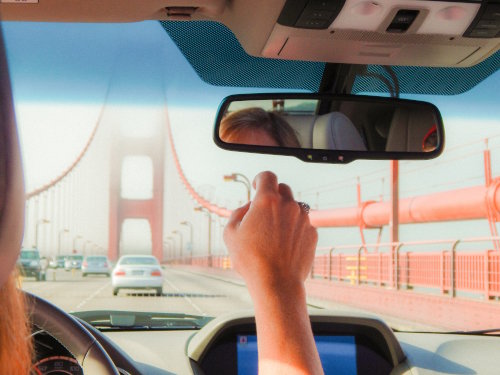 Woman driving over the Golden Gate Bridge while adjusting the review mirror