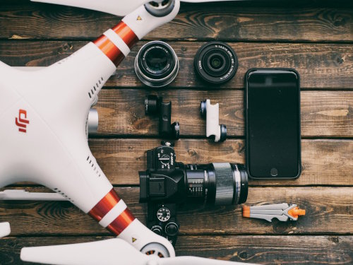 Electronic gadgets (4 lenses, a camera, smartphone and drone) resting on a wooden table