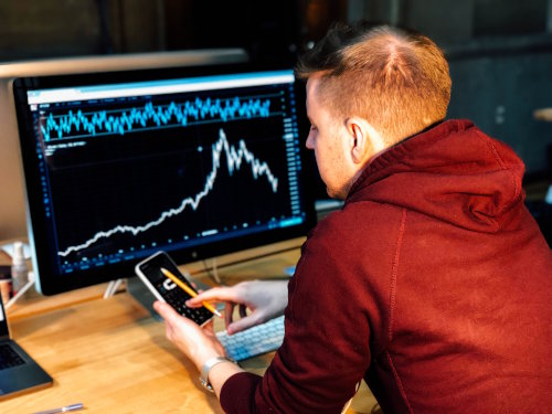 Man using calculator in front of monitor with stock charts