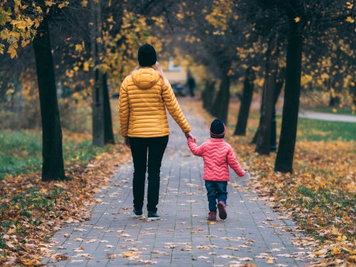 Mother and daughter, walking hand-in-hand on a tree-lined path